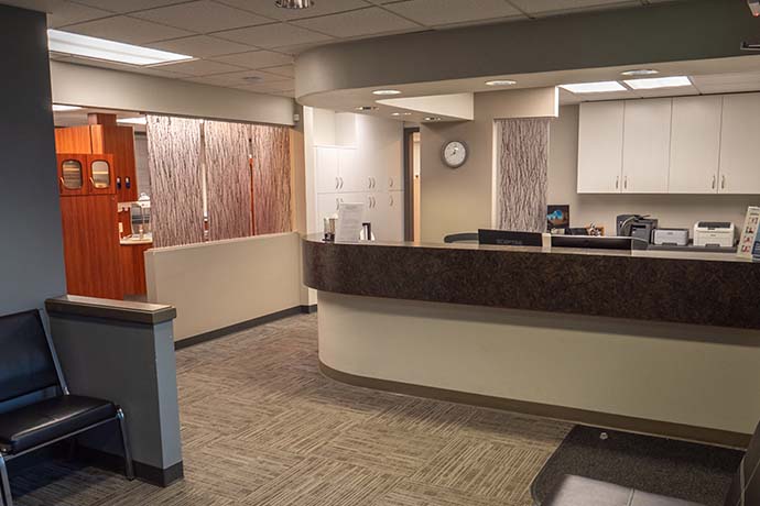 Reception area of a medical or dental office with a curved counter, seating, cabinets, and neutral-toned decor.