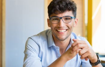 Closeup shot of young man wearing spectacle. Portrait of a guy with shirt and eyeglasses looking at camera indoor. Handsome smiling young man wearing blue spectacle.