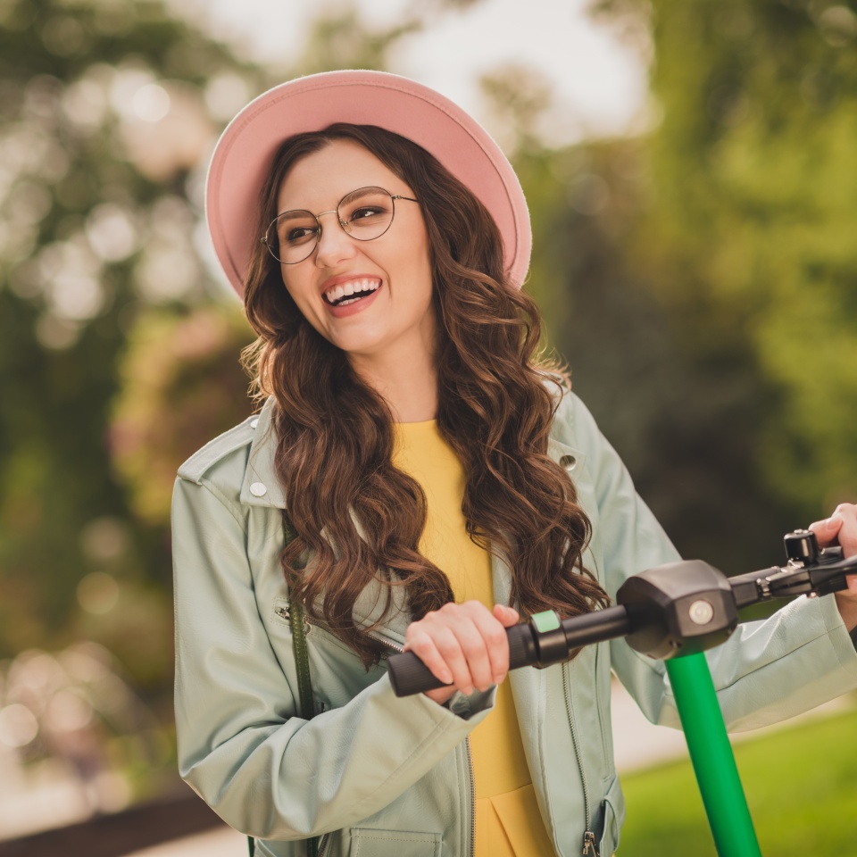 Photo of young happy smiling positive good mood lovely pretty girl in glasses and pink hat ride scooter outside in park