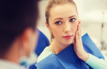 people, medicine, stomatology and health care concept - woman patient talking to male dentist and complain of toothache at dental clinic office