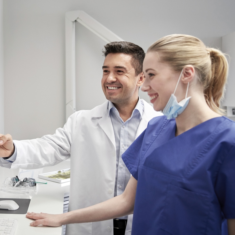 people, medicine, stomatology, technology and health care concept - happy dentists looking to x-ray scan on monitor at dental clinic