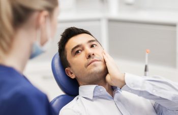 people, medicine, stomatology and health care concept - male patient with toothache complaining to female dentist at dental clinic office