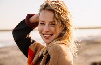 Happy young white woman smiling while walking by seashore on sunny day
