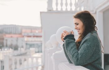 Beautiful smiling woman relaxing and drinking coffee on the balcony in the morning